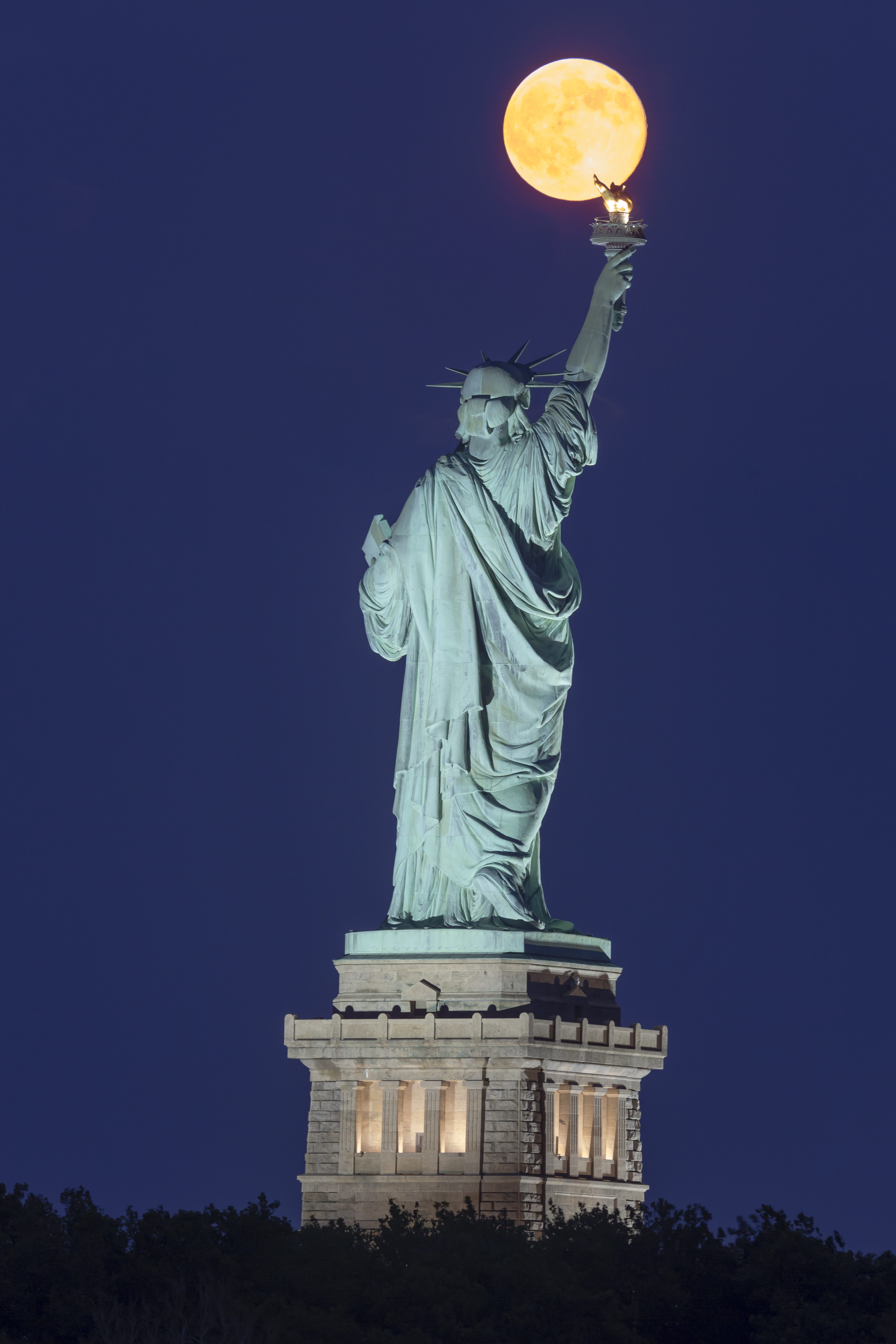 The super moon rises over the Statue of Liberty during the blue hour after sunset.